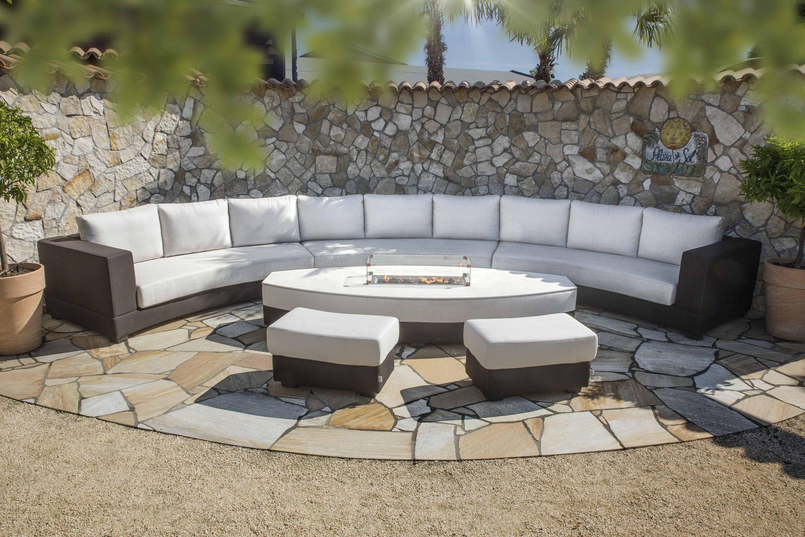 Ronde all weather loungebank met poefs rond een ovale vuurtafel op een natuurstenen terras